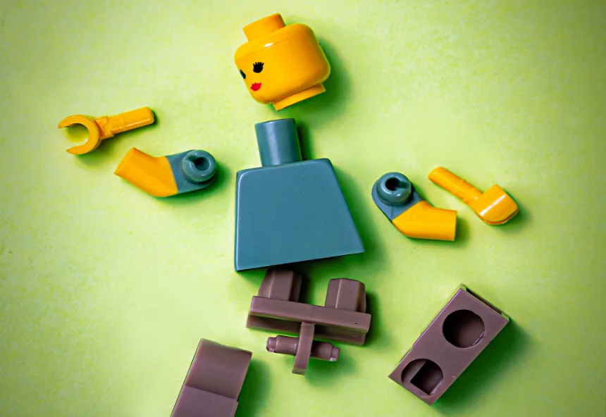 A disassembled toy figure with its head, arms, and body scattered apart, representing the brokenness of church hurt