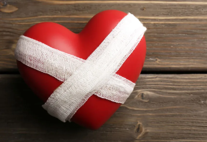 A red heart wrapped in white bandages resting on weathered wood, a picture of a wounded heart beginning to heal
