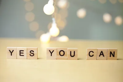Wooden letter tiles spelling YES YOU CAN in front of warm, glowing lights