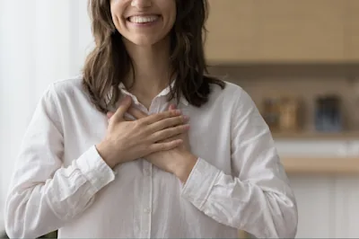 A smiling woman resting both hands gently over her heart in gratitude and peace