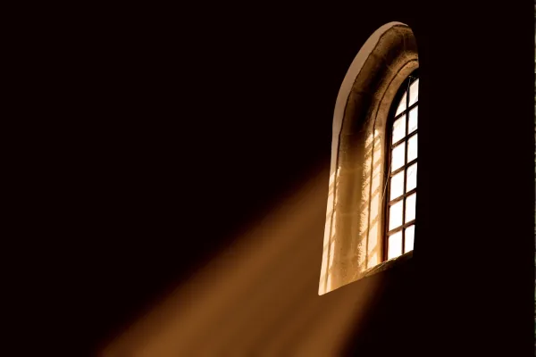 Warm light streaming through an arched church window into a darkened sanctuary